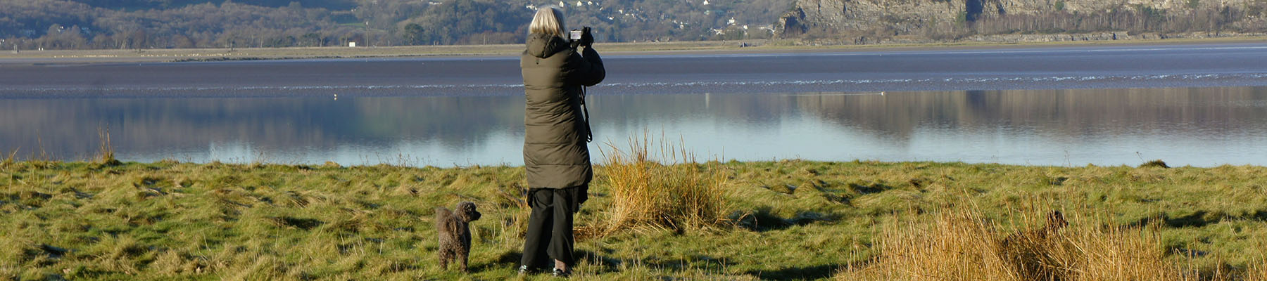 Woman walking her dog and taking a photo of a lake in Lancashire.